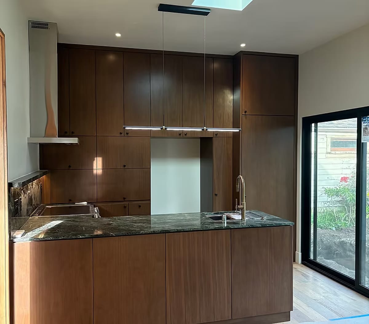 A compact walnut kitchen with a green marble counter and a sliding door onto the garden