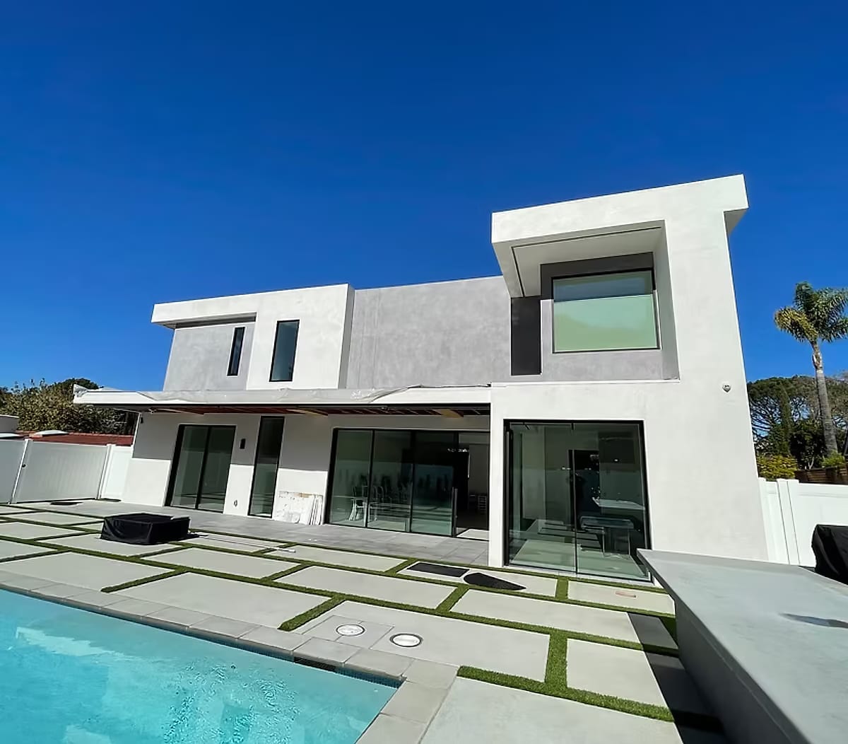 The rear elevation of a new two-story home with sliding glass doors opening onto a paver terrace and pool