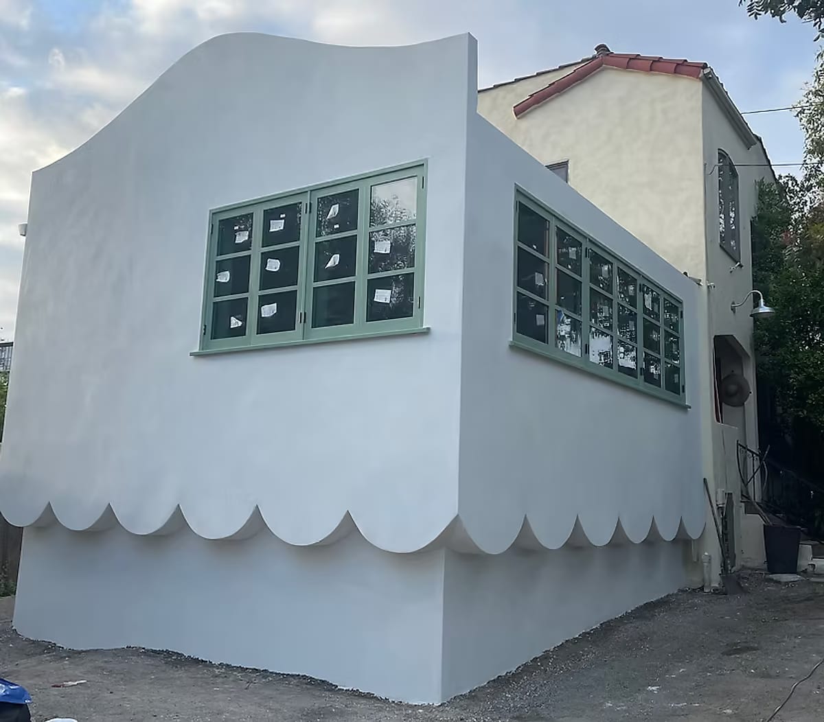 A rear structure re-clad in pale stucco with a scalloped skirt and sage-green steel-framed windows